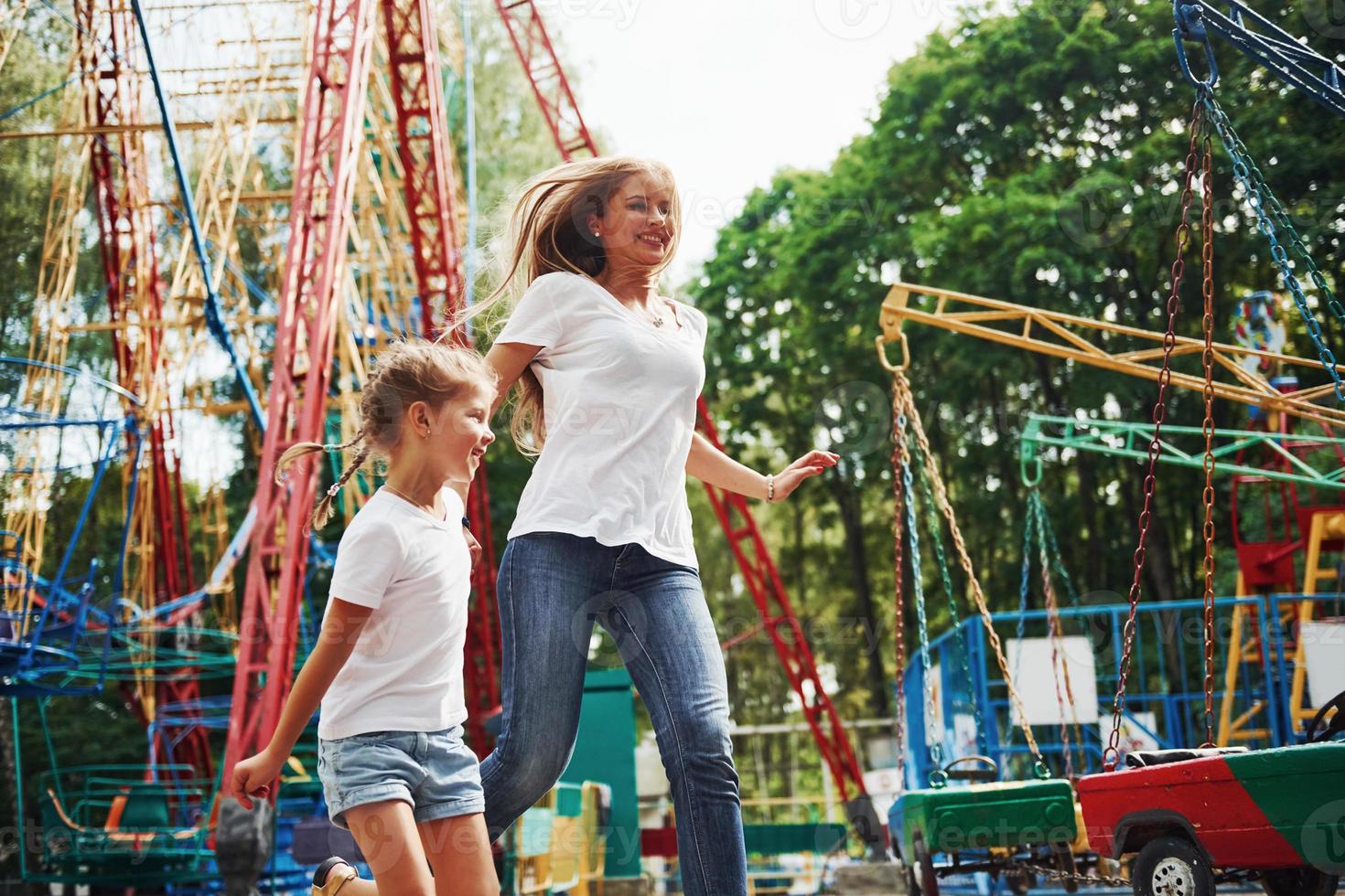 Running and playing. Cheerful little girl her mother have a good time in the park together near attractions photo