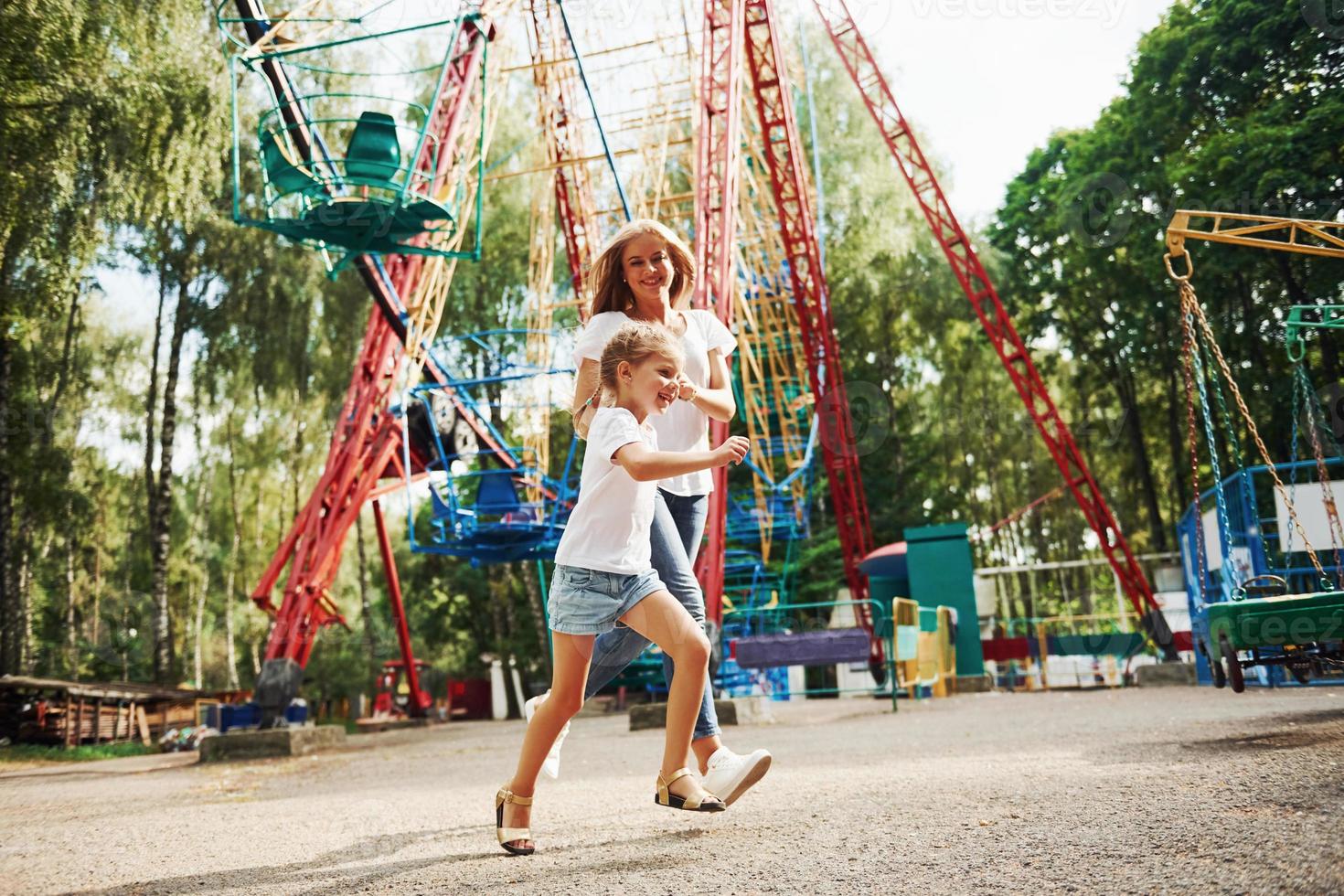 Running and playing. Cheerful little girl her mother have a good time in the park together near attractions photo