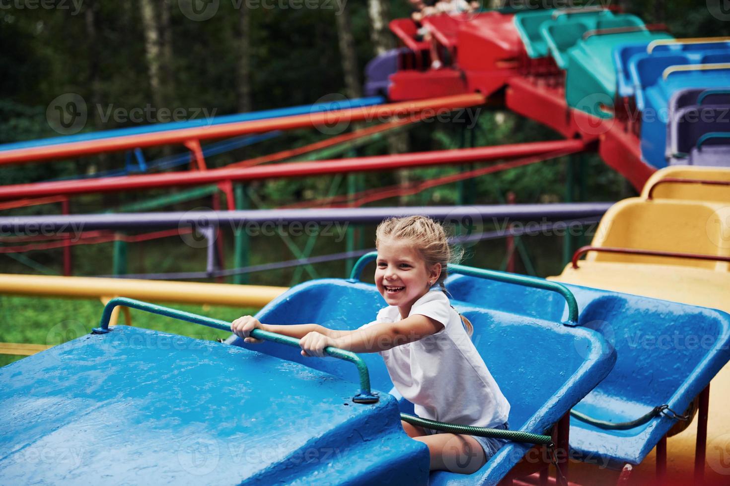 Happy female kid have fun on a roller coaster in the park at daytime photo