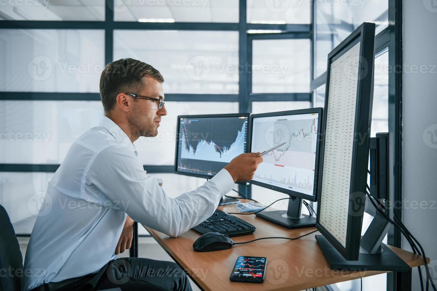 Analysing graphs. Young businessman in formal clothes is in office with multiple screens. Conception of exchange and money photo