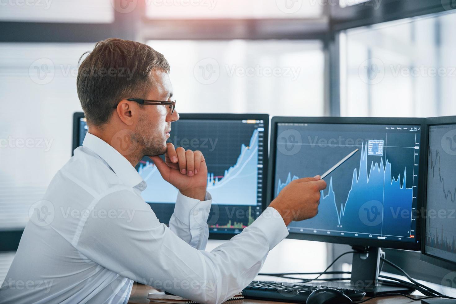 Monitoring information. Young businessman in formal clothes is in office with multiple screens. Conception of exchange and money photo