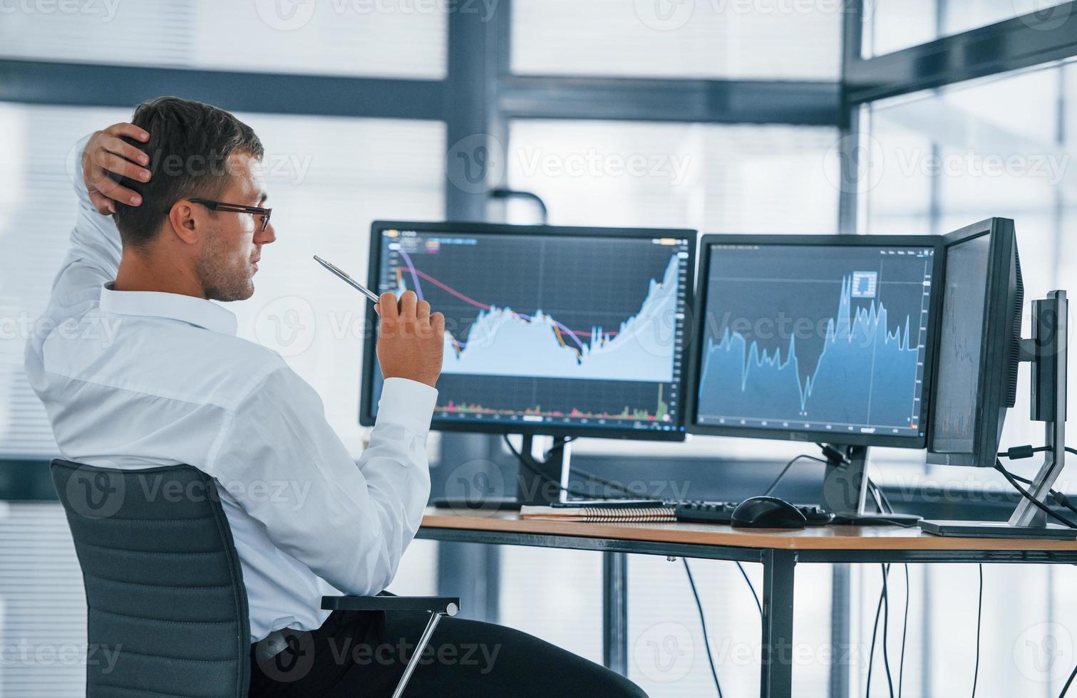 Monitoring information. Young businessman in formal clothes is in office with multiple screens. Conception of exchange and money photo