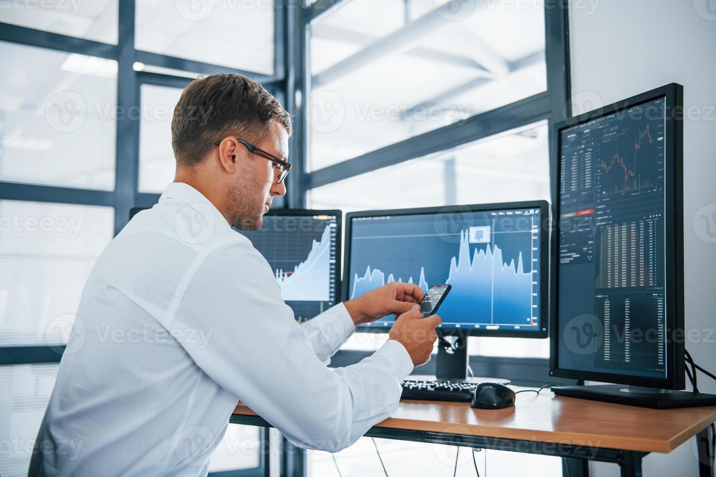 Searching information. Young businessman in formal clothes is in office with multiple screens. Conception of exchange and money photo