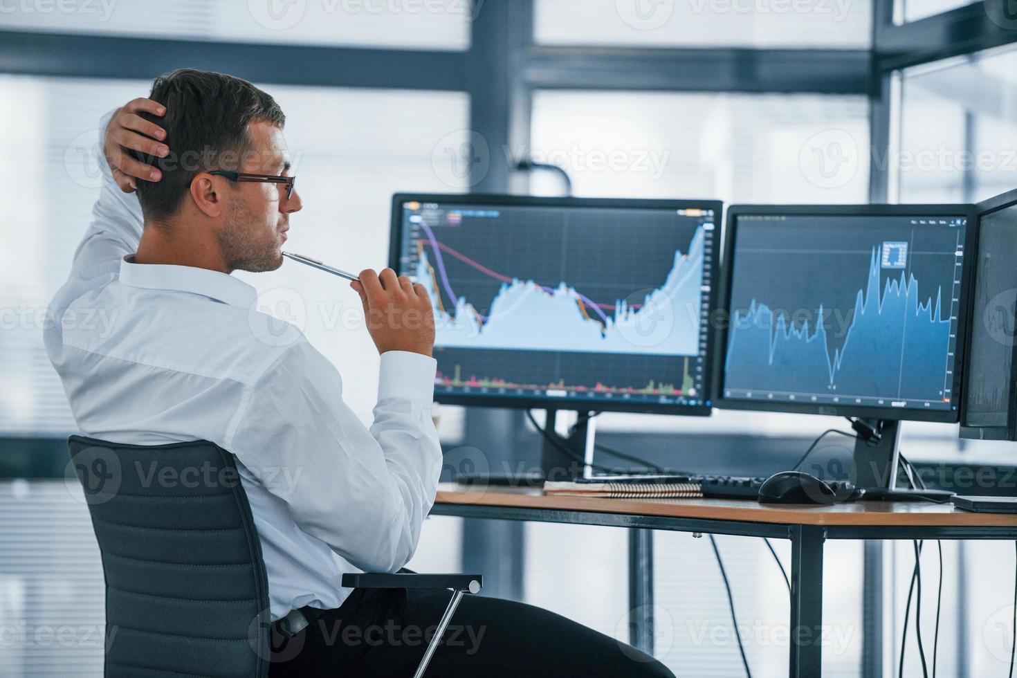 Monitoring information. Young businessman in formal clothes is in office with multiple screens. Conception of exchange and money photo