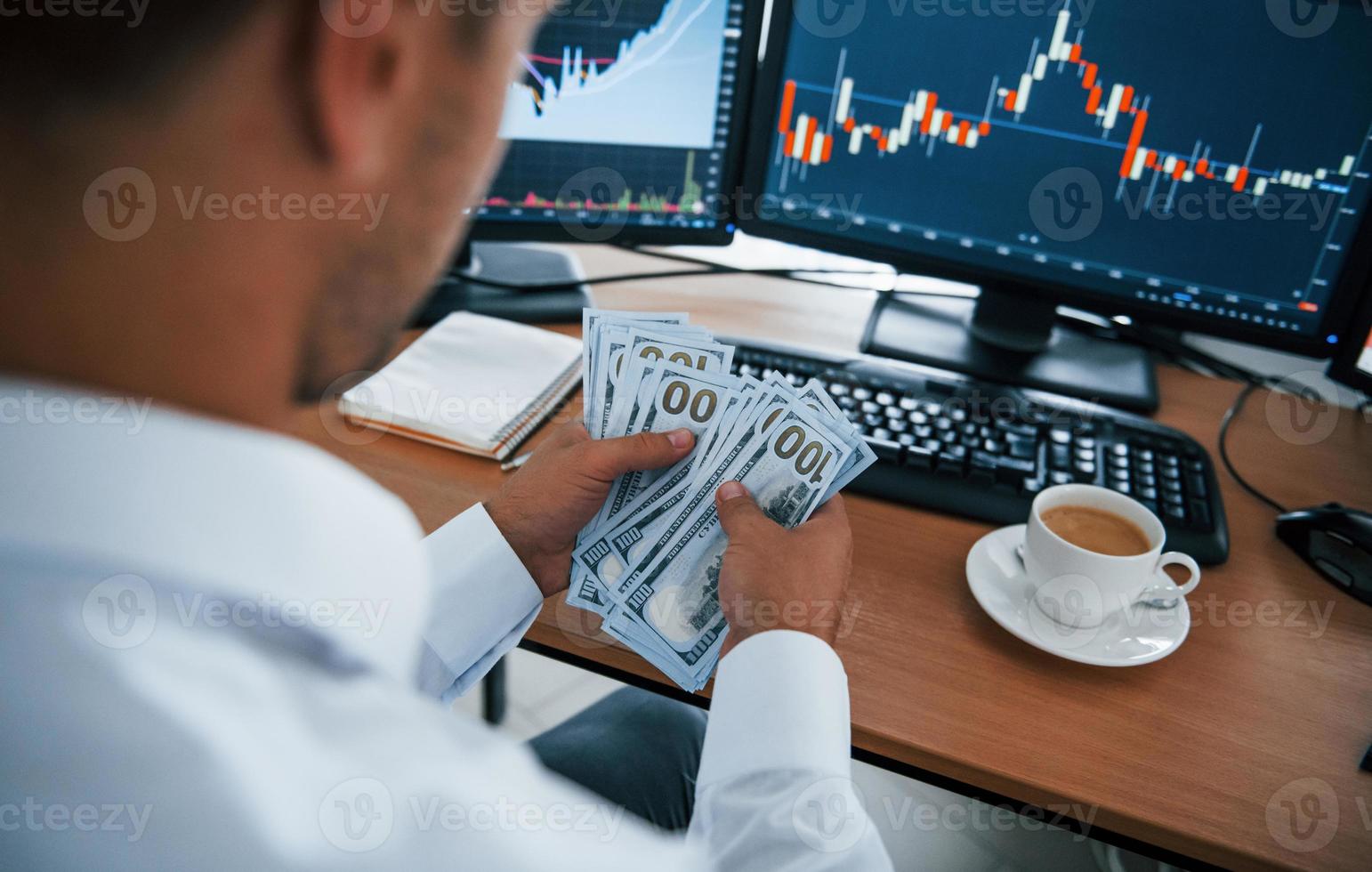 Calculating money. Young businessman in formal clothes is in office with multiple screens. Conception of exchange and money photo