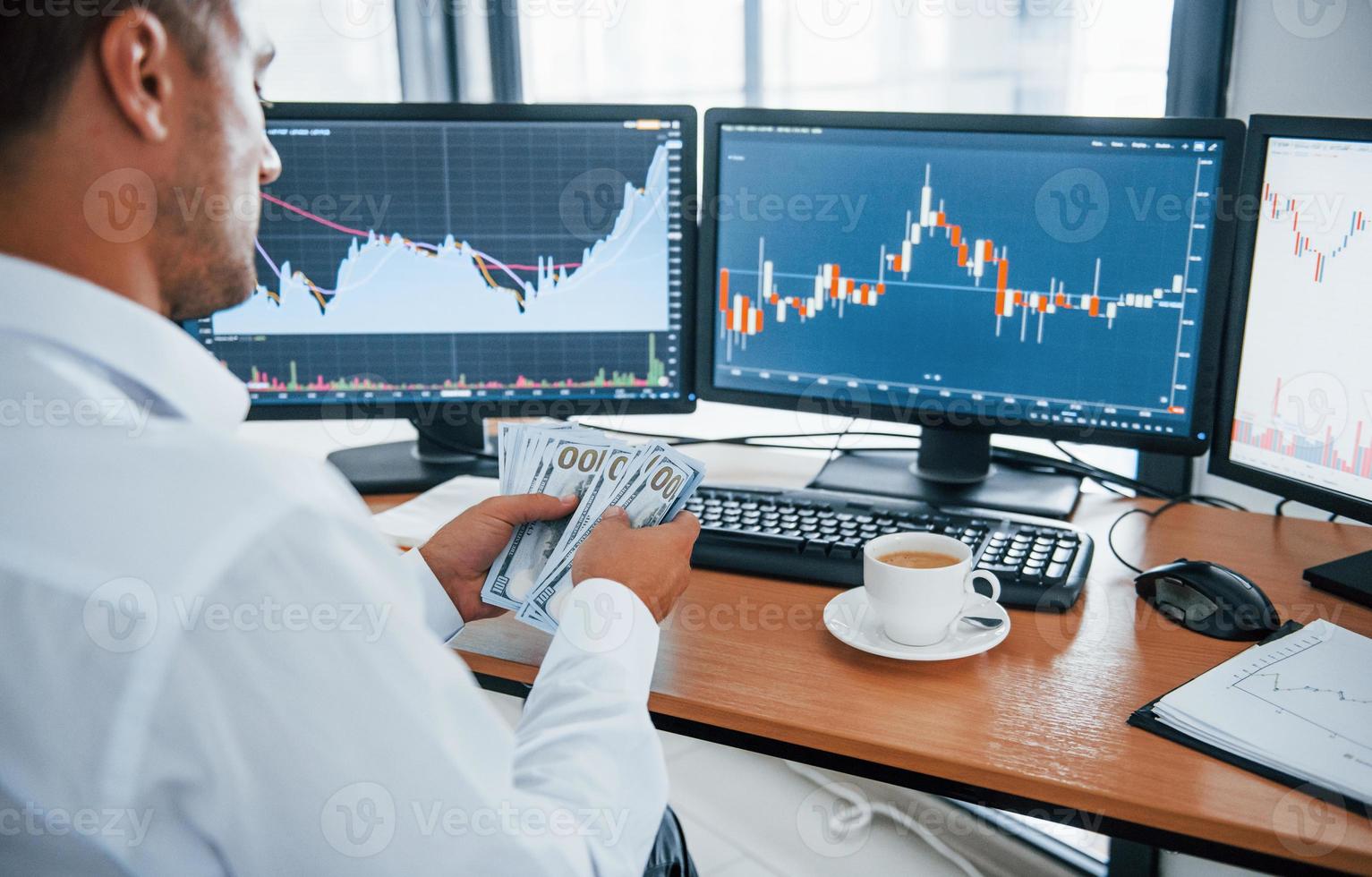 Calculating money. Young businessman in formal clothes is in office with multiple screens. Conception of exchange and money photo