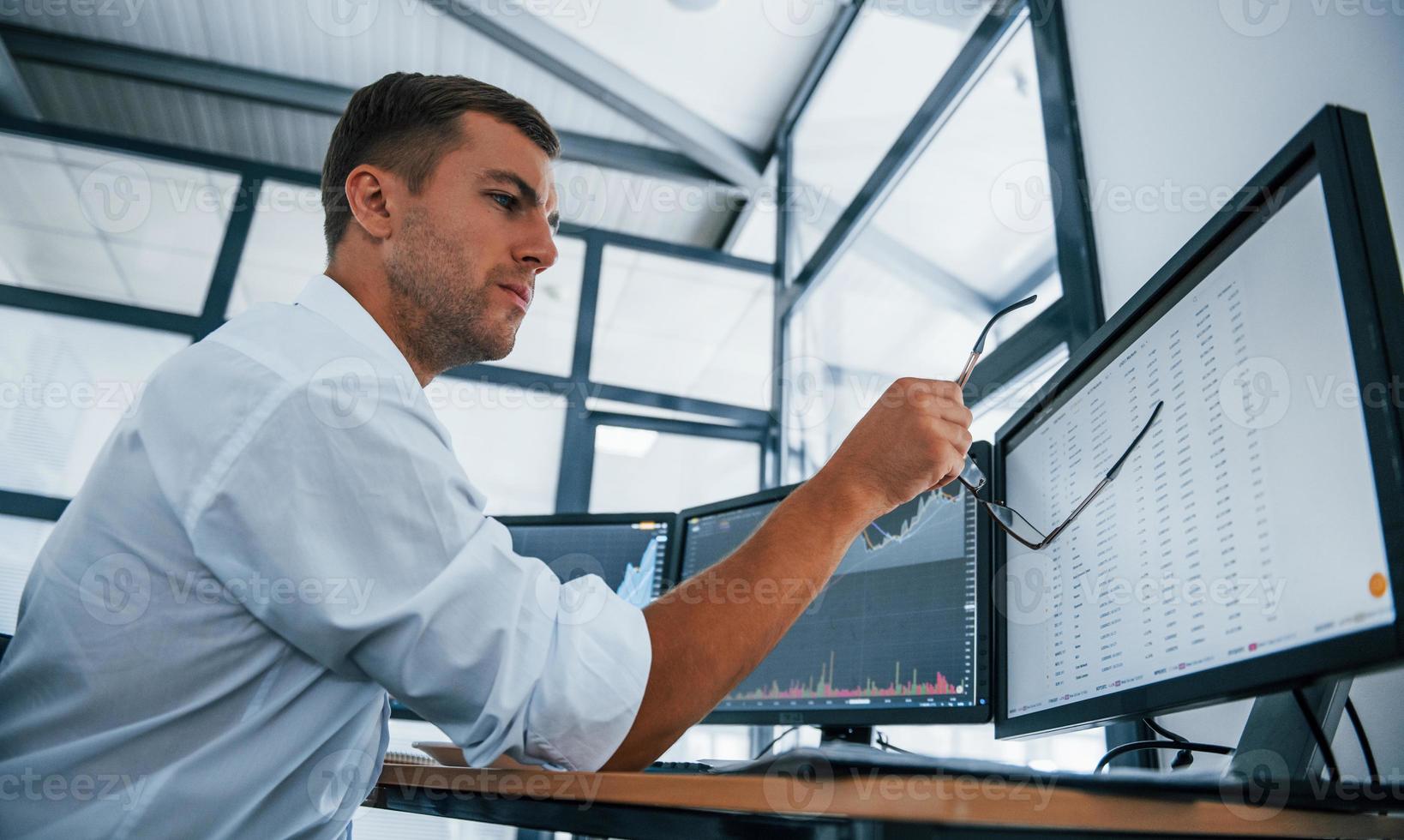 Concentrated at work. Young businessman in formal clothes is in office with multiple screens. Conception of exchange and money photo