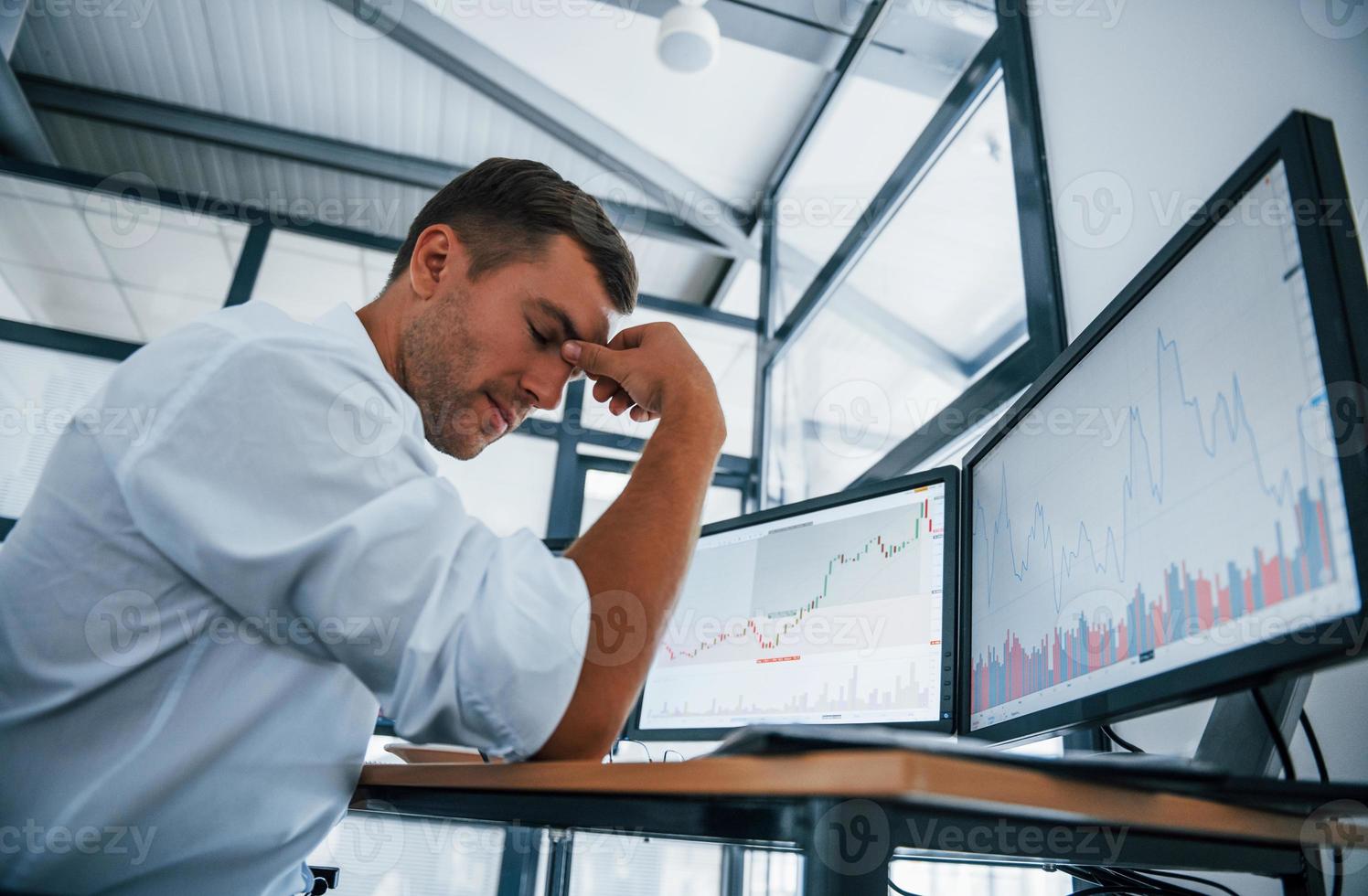 Feeling sad. Failure and depression. Young businessman in formal clothes is in office with multiple screens. Conception of exchange and money photo