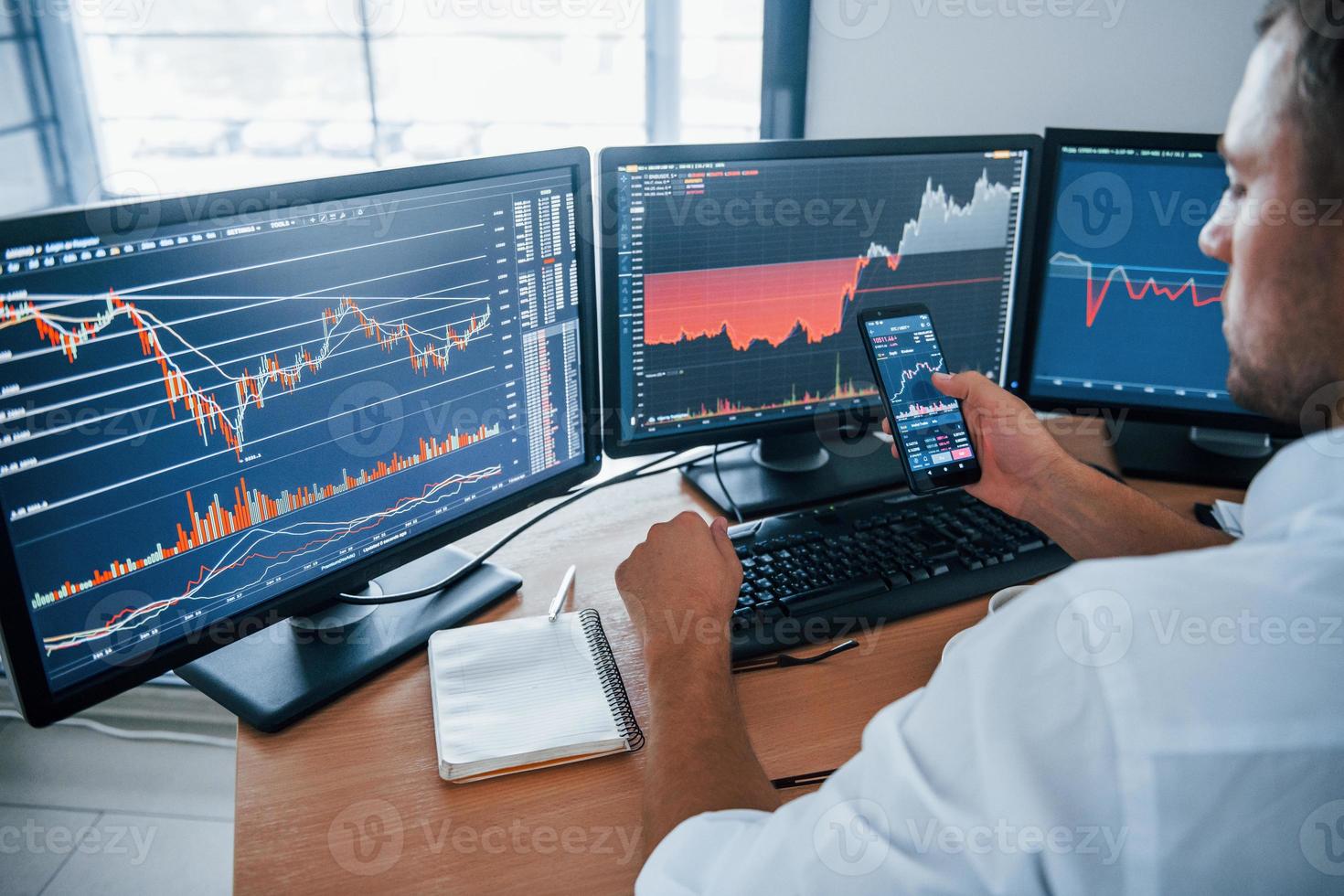 Young businessman in formal clothes is in office with multiple screens. Conception of exchange and money photo