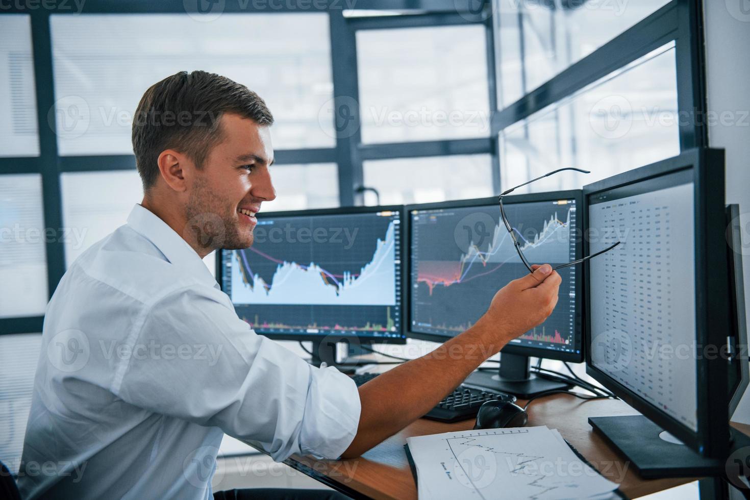 Concentrated at work. Young businessman in formal clothes is in office with multiple screens. Conception of exchange and money photo