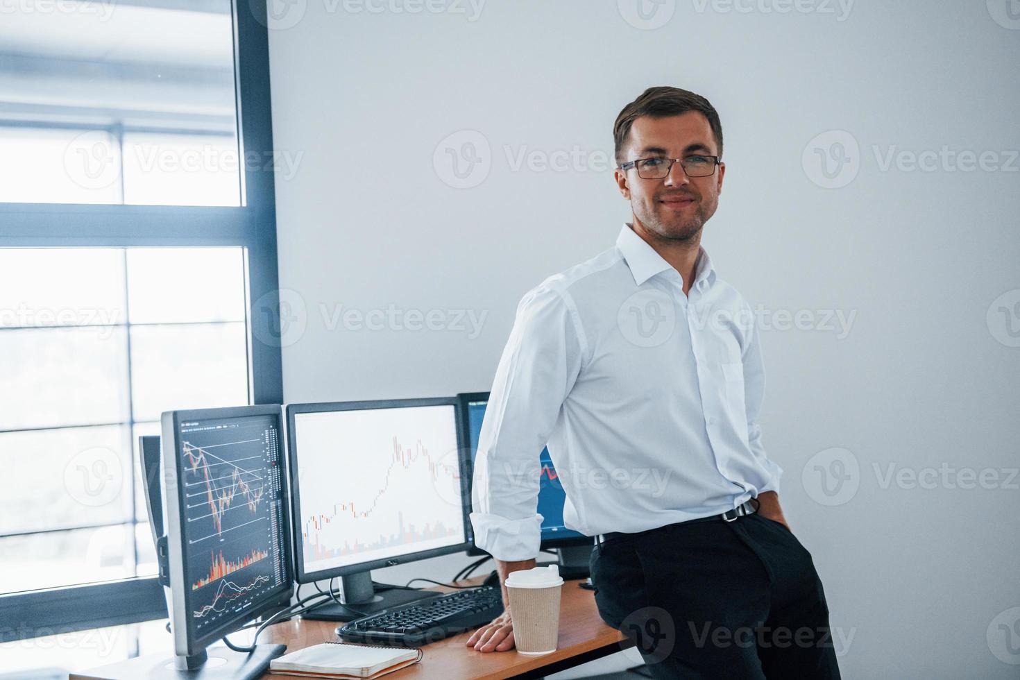 Happy employee. Young businessman in formal clothes is in office with multiple screens. Conception of exchange and money photo