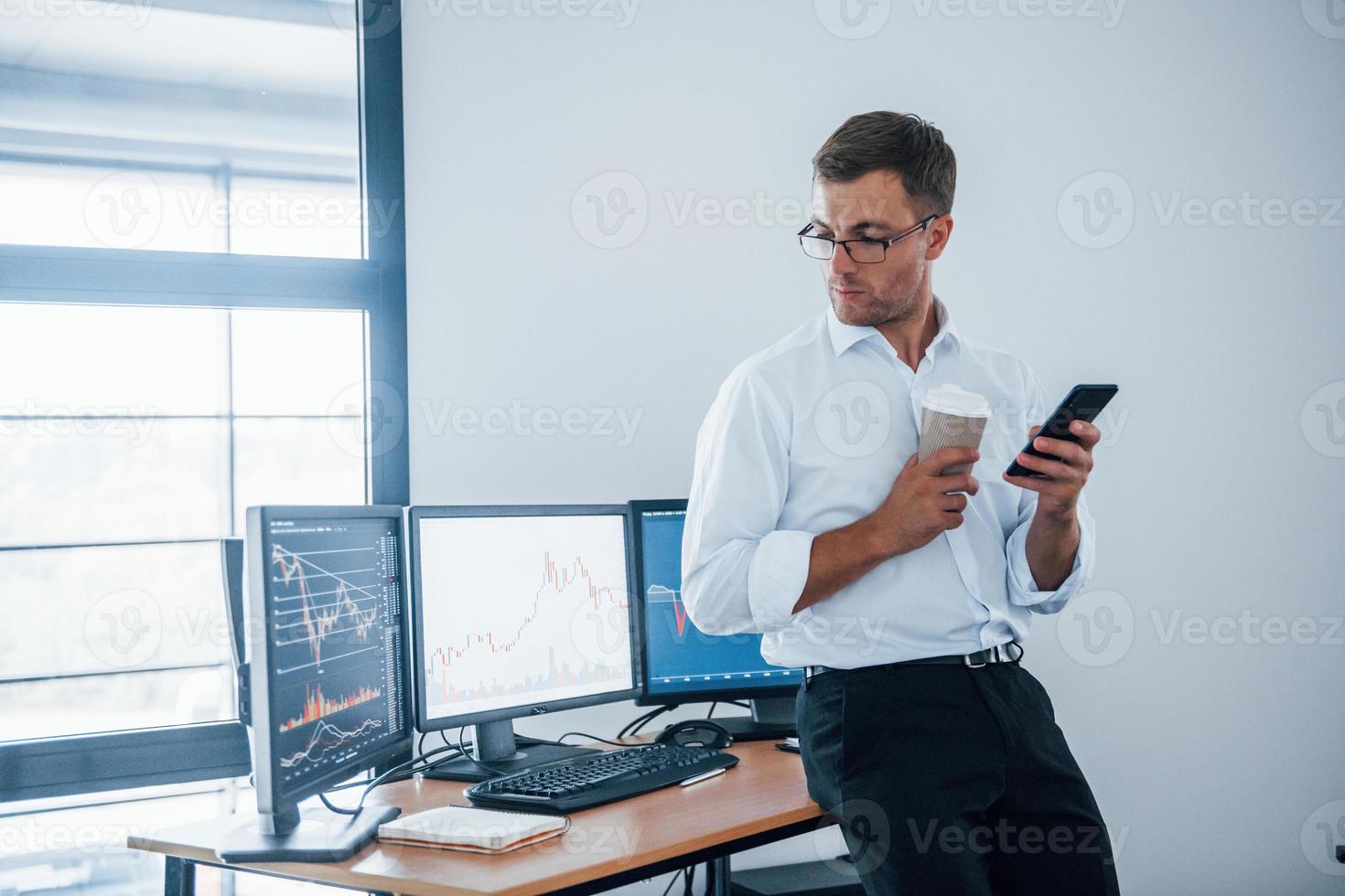 Taking fresh drink. Young businessman in formal clothes is in office with multiple screens. Conception of exchange and money photo