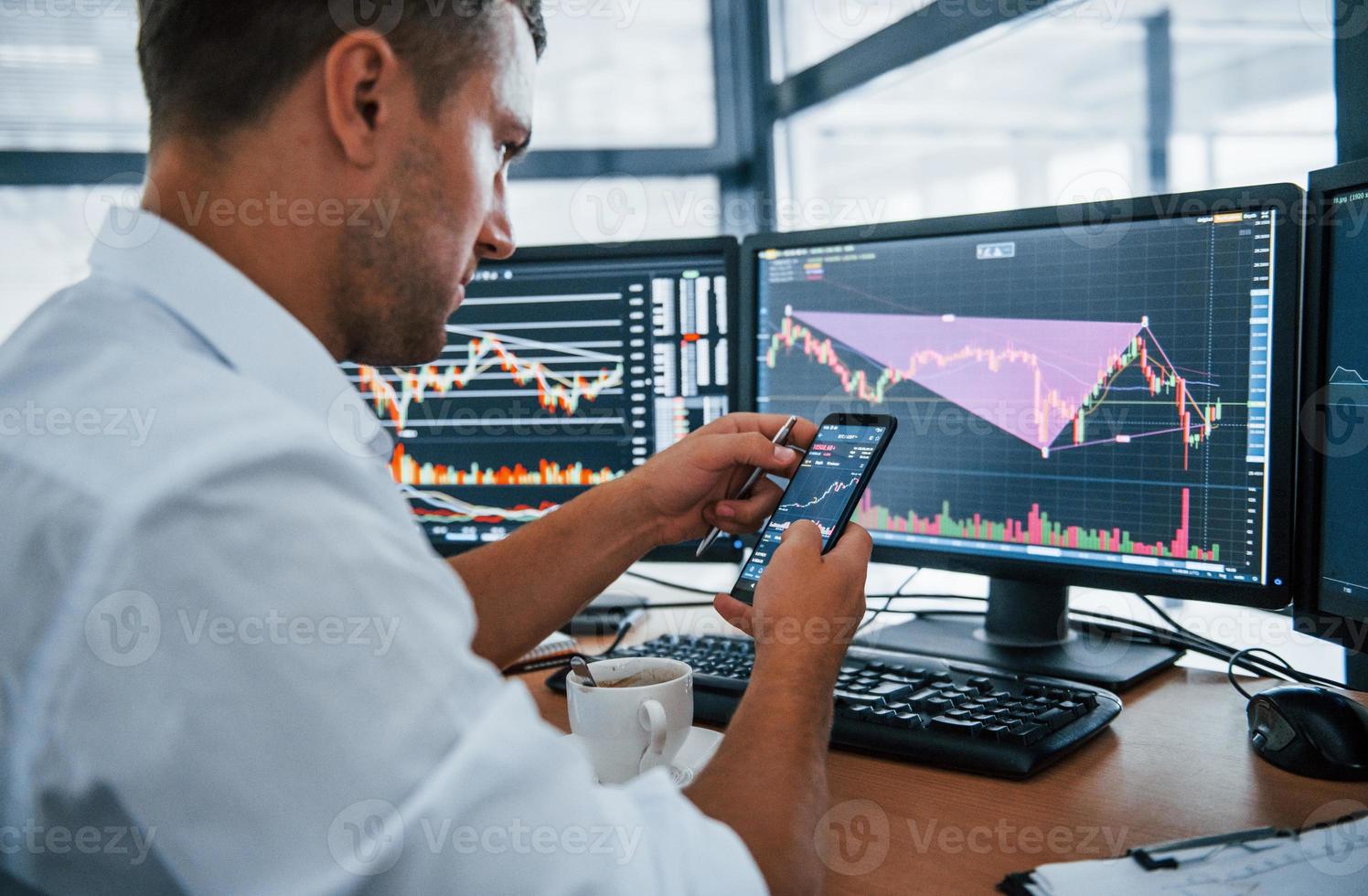 Young businessman in formal clothes is in office with multiple screens. Conception of exchange and money photo