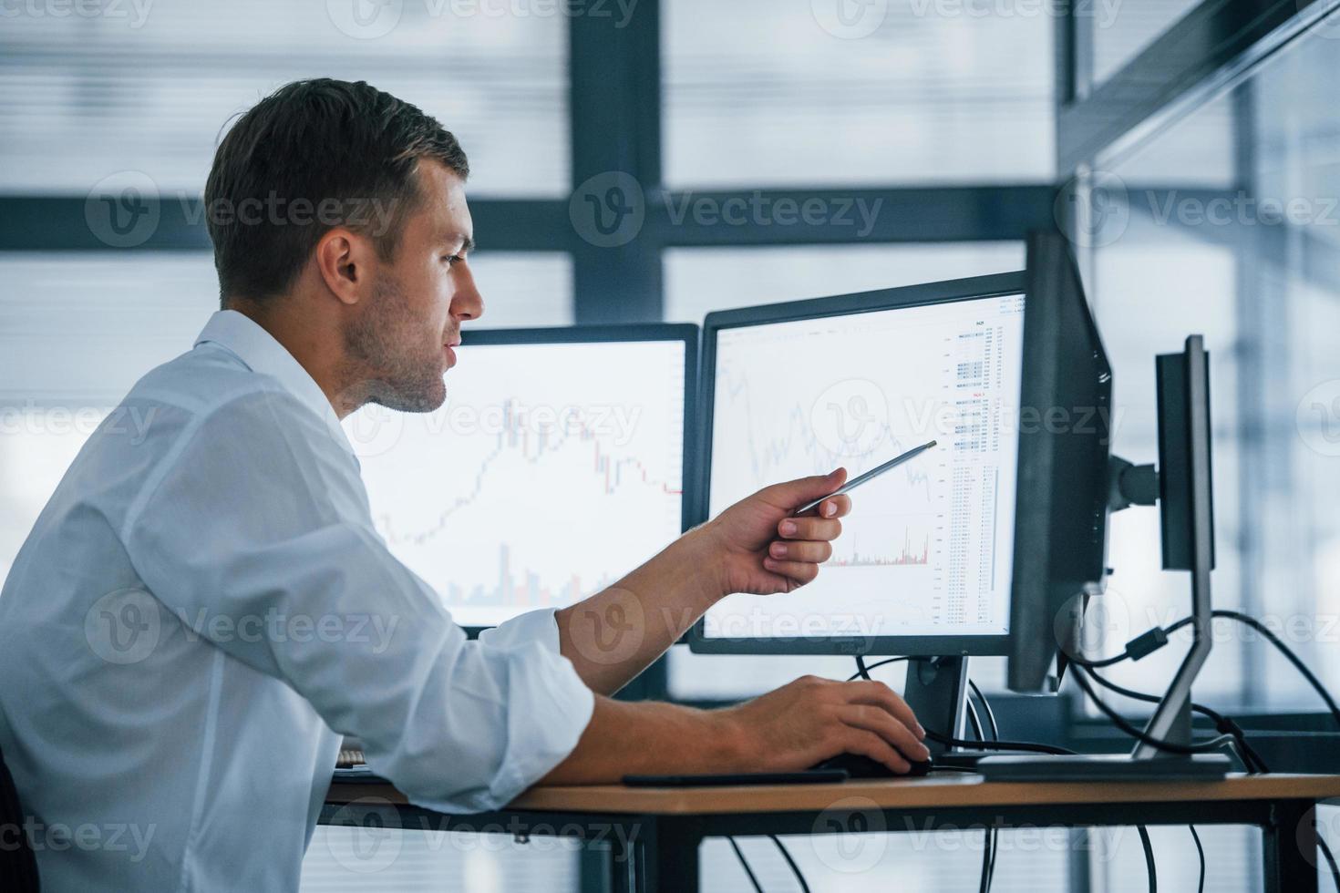 Side view. Young businessman in formal clothes is in office with multiple screens. Conception of exchange and money photo