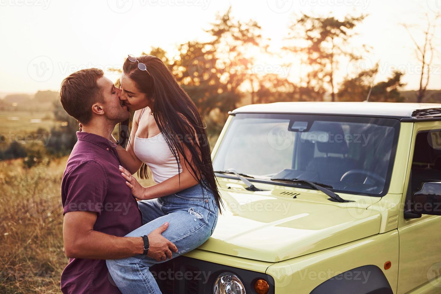 encantadora pareja besándose al aire libre. la chica se sienta en un jeep verde. hermosa tarde soleada foto