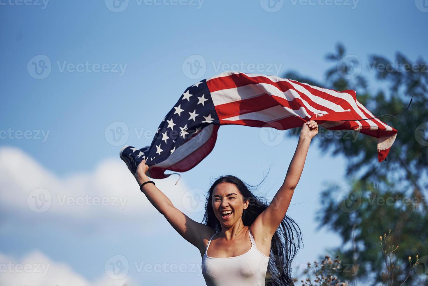 Female patriot runs with USA flag in hands outdoors in the field against blue sky photo