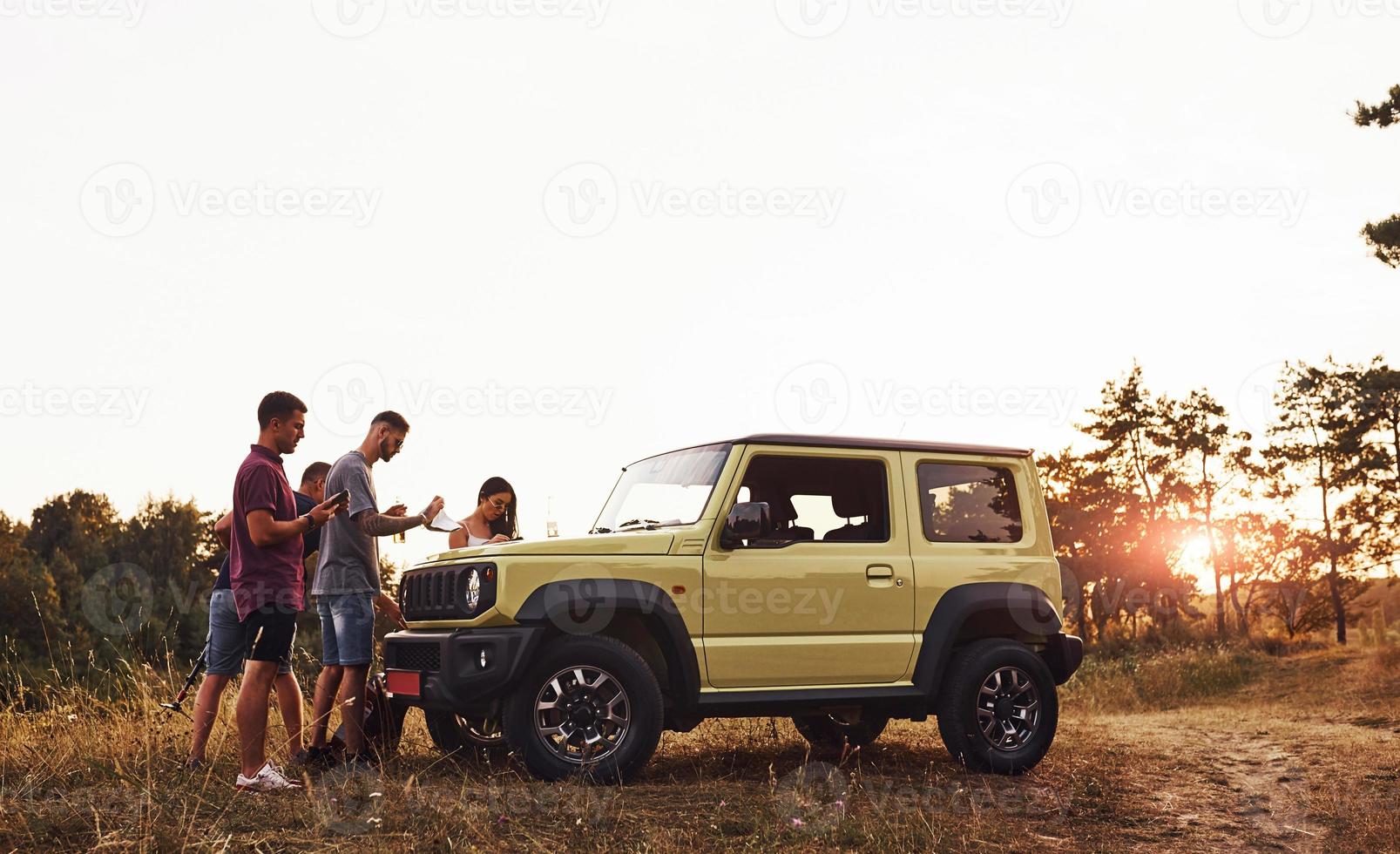 Beautiful nature. Group of cheerful friends have nice weekend at sunny day near theirs green car outdoors photo