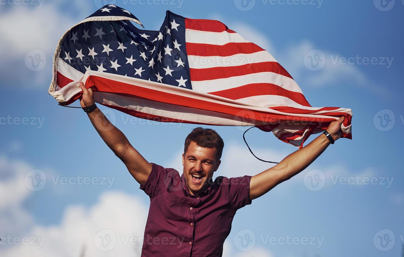 Patriotic happy man waving American Flag against cloudy blue sky photo