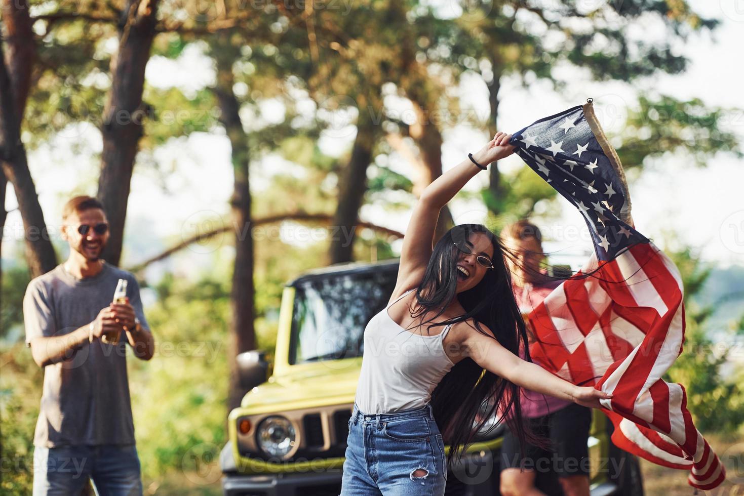 In the forest. Friends have nice weekend outdoors near theirs green car with USA flag photo