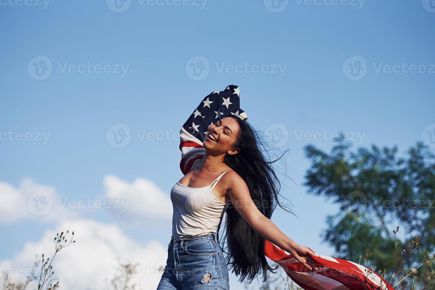 Female patriot runs with USA flag in hands outdoors in the field against blue sky photo