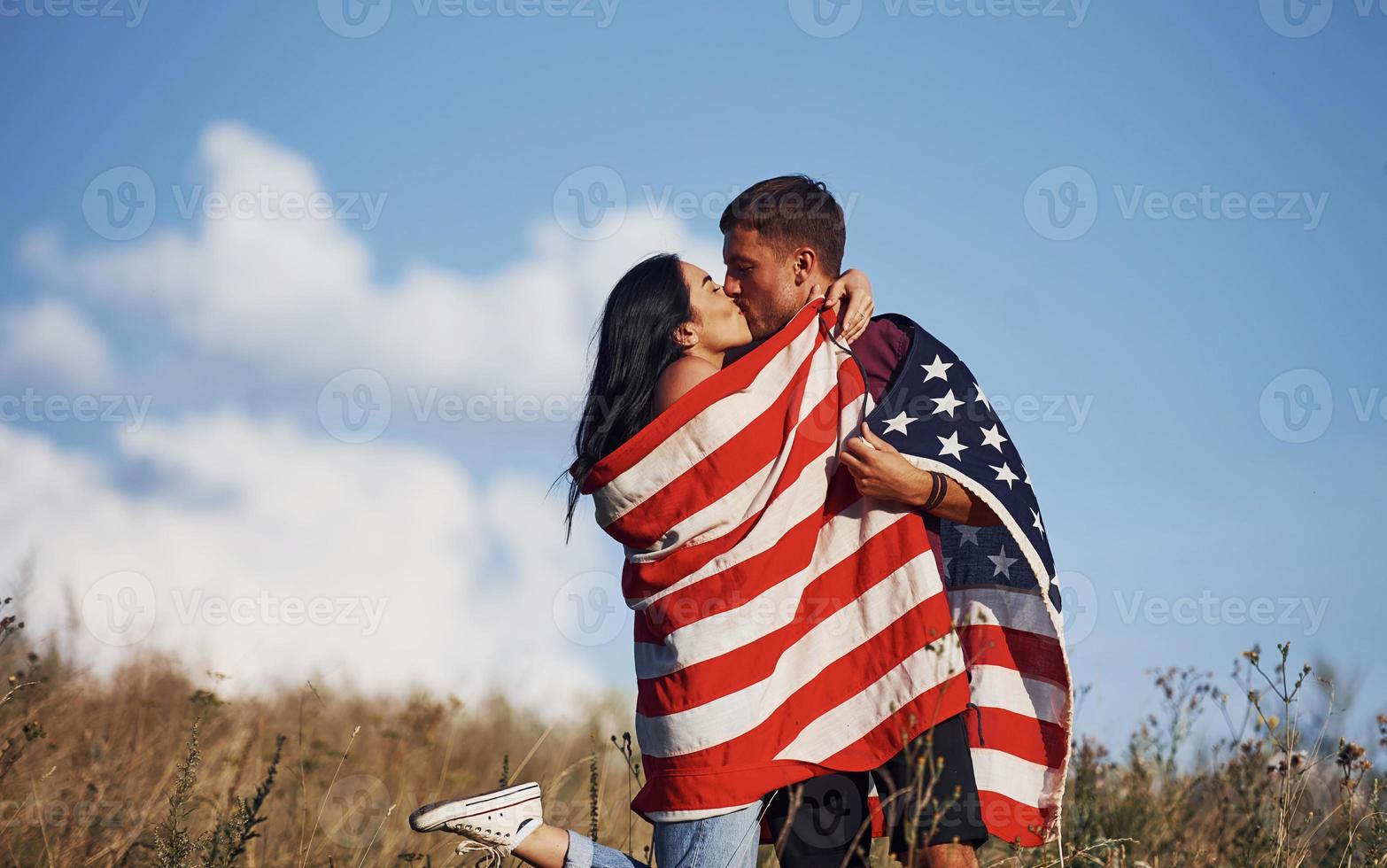 Kissing each other. Feels freedom. Beautiful couple with American Flag have a good time outdoors in the field photo