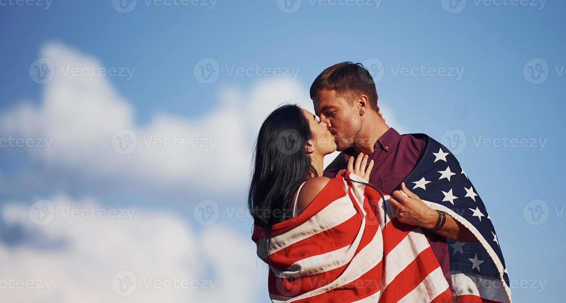 besándonos. siente libertad. hermosa pareja con bandera americana pasar un buen rato al aire libre en el campo foto
