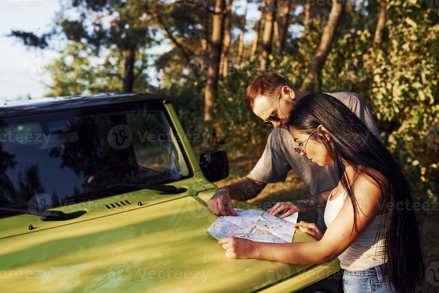 jóvenes amigos leyendo el mapa que está en el capó del moderno jeep verde en el bosque foto