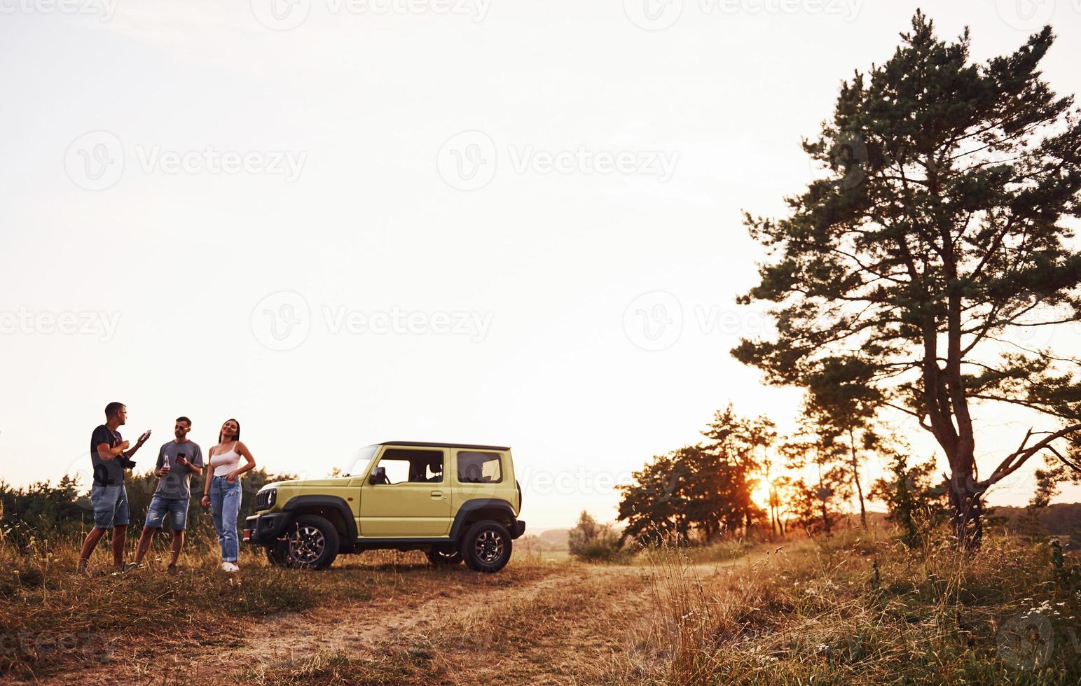 escena rural. grupo de amigos alegres que tengan un buen fin de semana en un día soleado cerca de su auto verde al aire libre foto