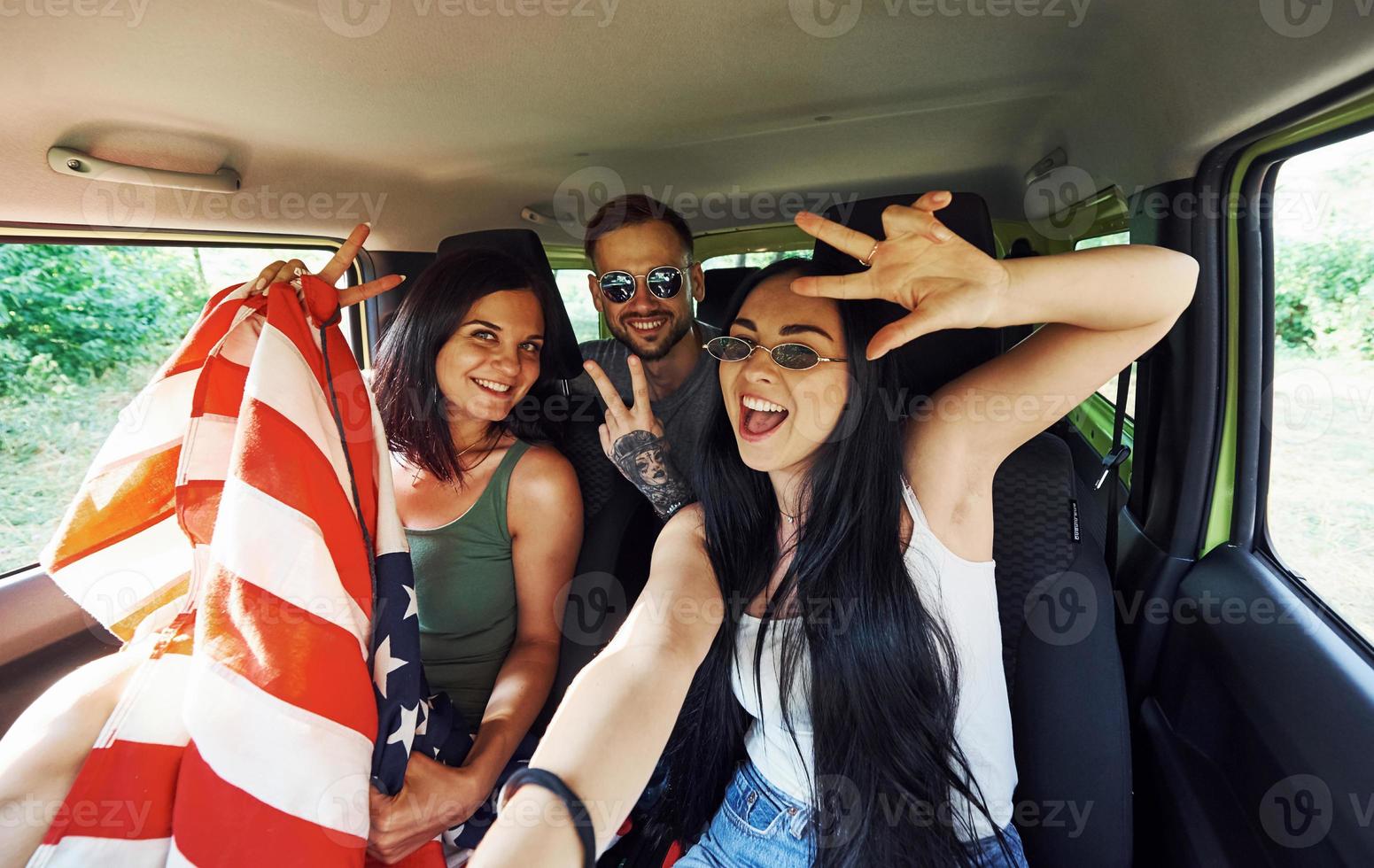 Friends making selfie when sits indoors with American Flag in hands photo