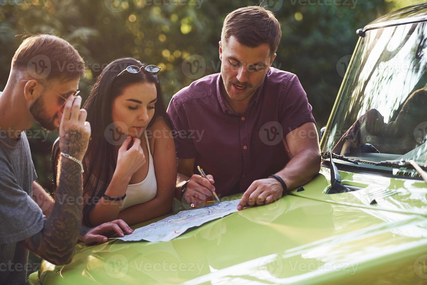 jóvenes amigos leyendo el mapa que está en el capó del moderno jeep verde en el bosque foto