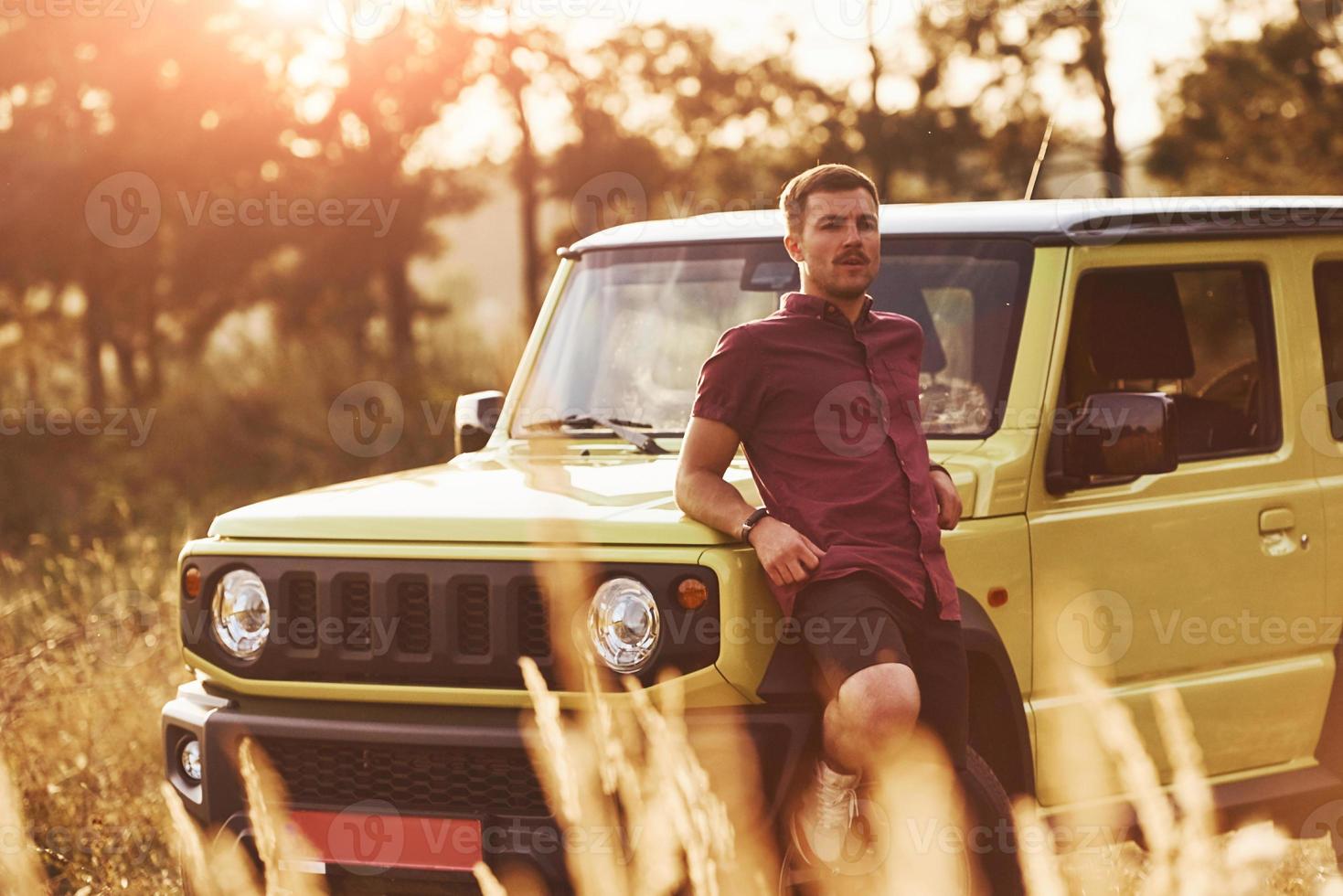 Portrait of man that leaning on green car at beautiful sunny day outdoors in the field photo