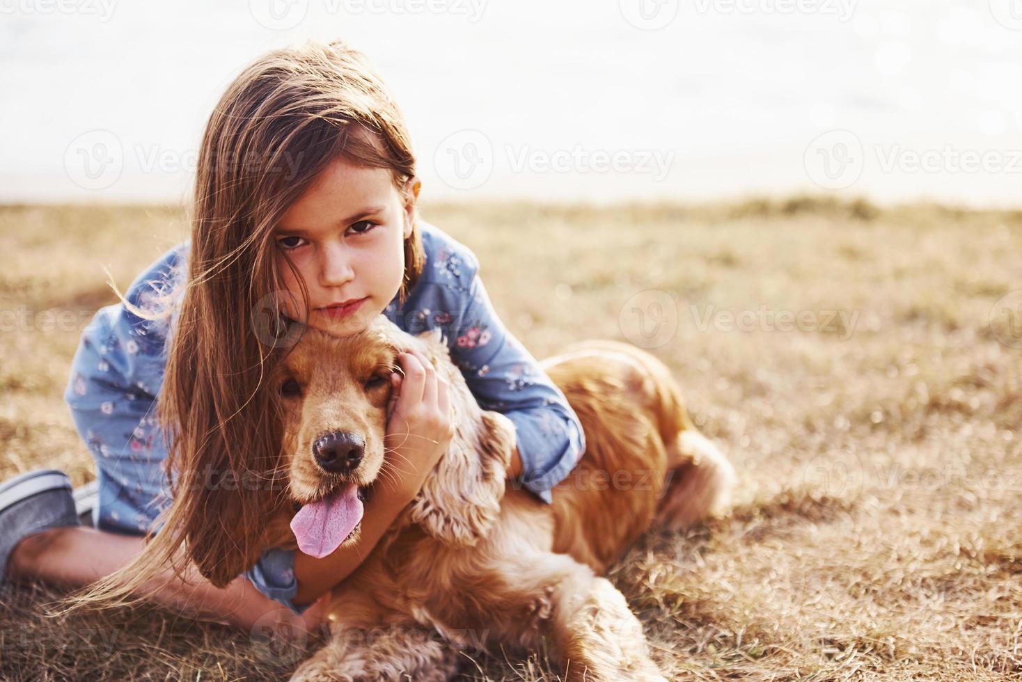 Resting near the lake. Cute little girl have a walk with her dog outdoors at sunny day photo