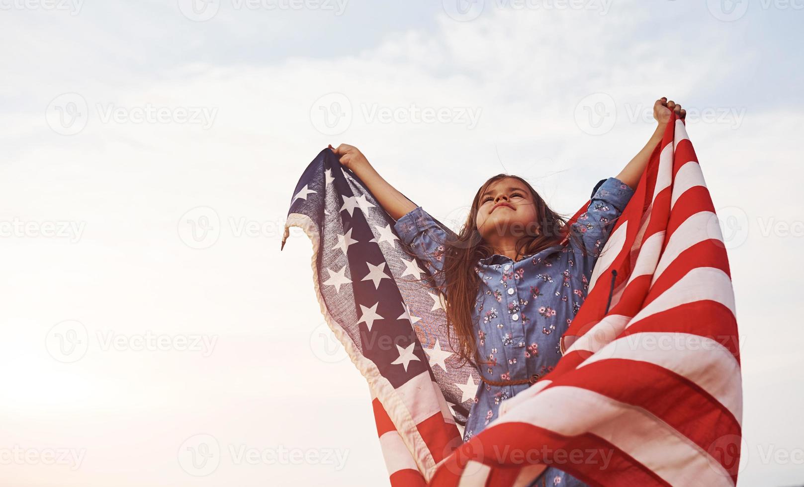 Patriotic female kid with American Flag in hands. Against cloudy sky photo