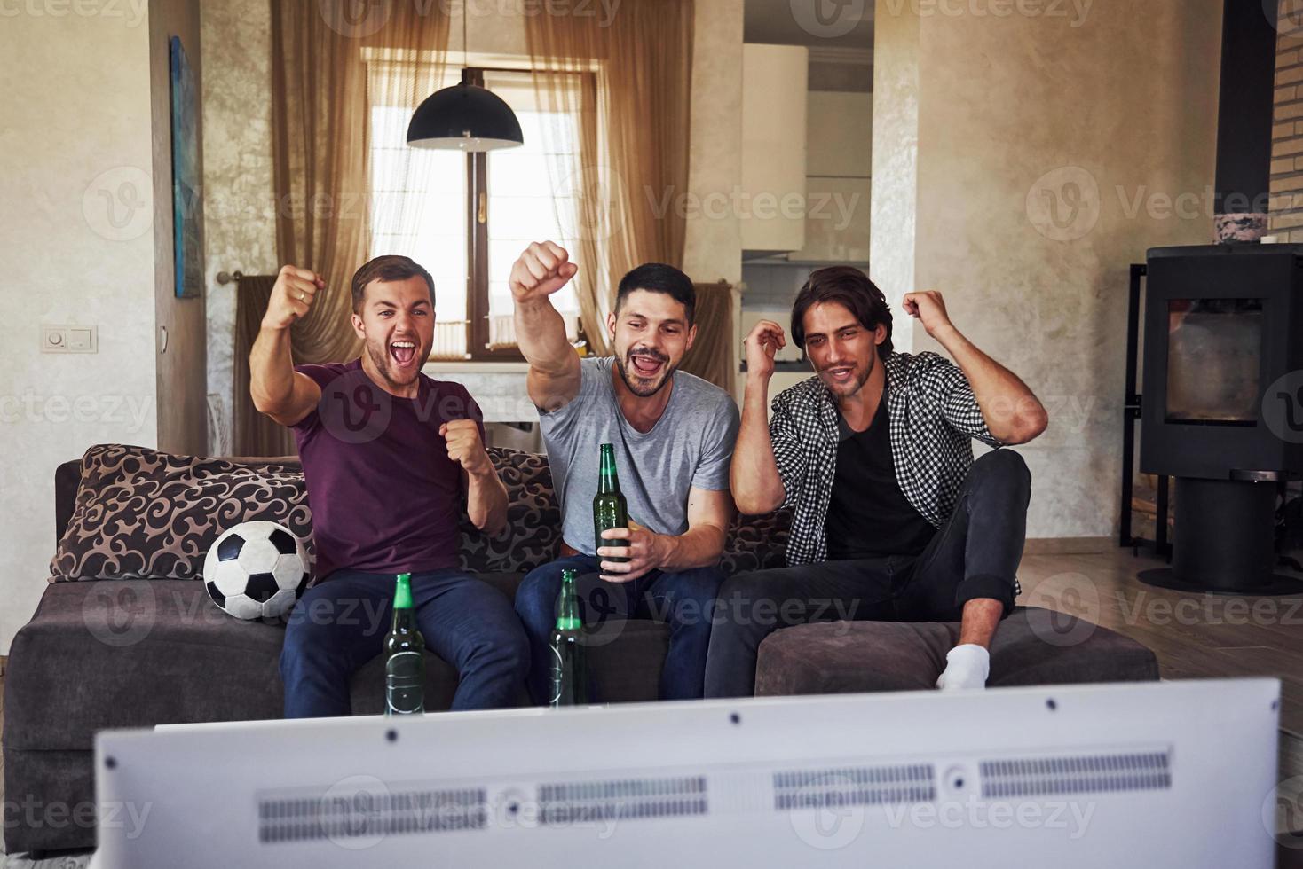 Excited three friends watching soccer on TV at home together photo