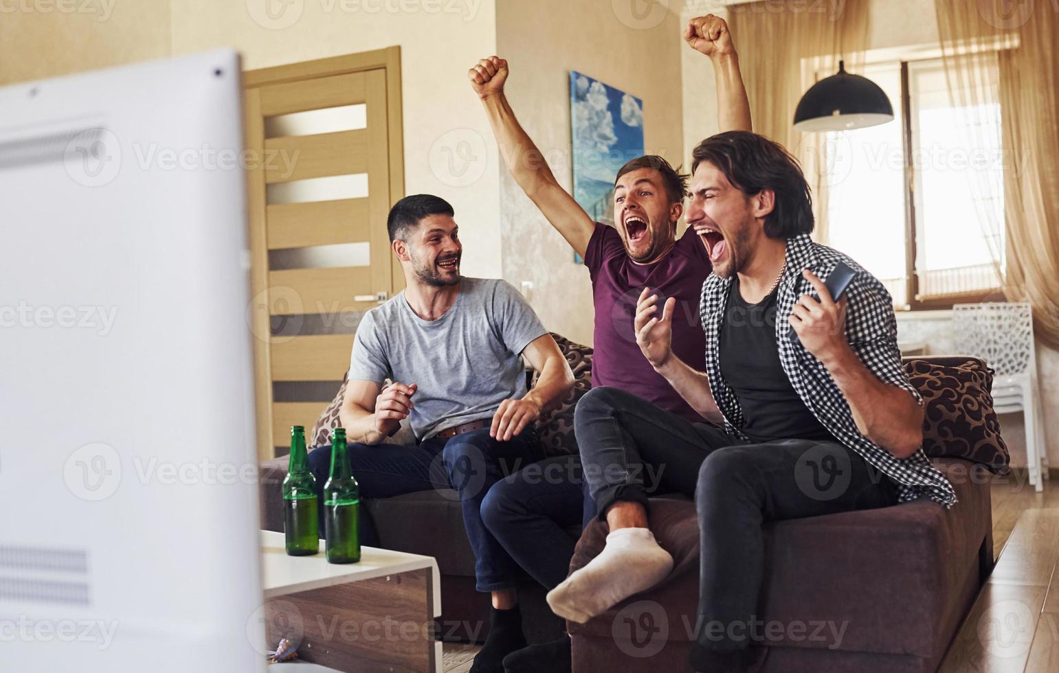 Celebrating victory. Excited three friends watching soccer on TV at home together photo
