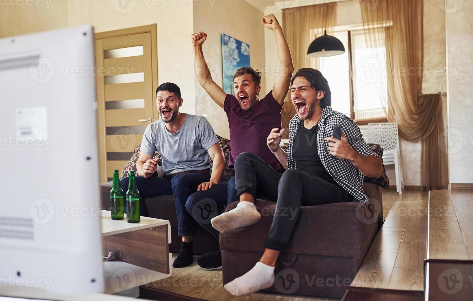 celebrando la victoria. emocionados tres amigos viendo fútbol en la televisión en casa juntos foto