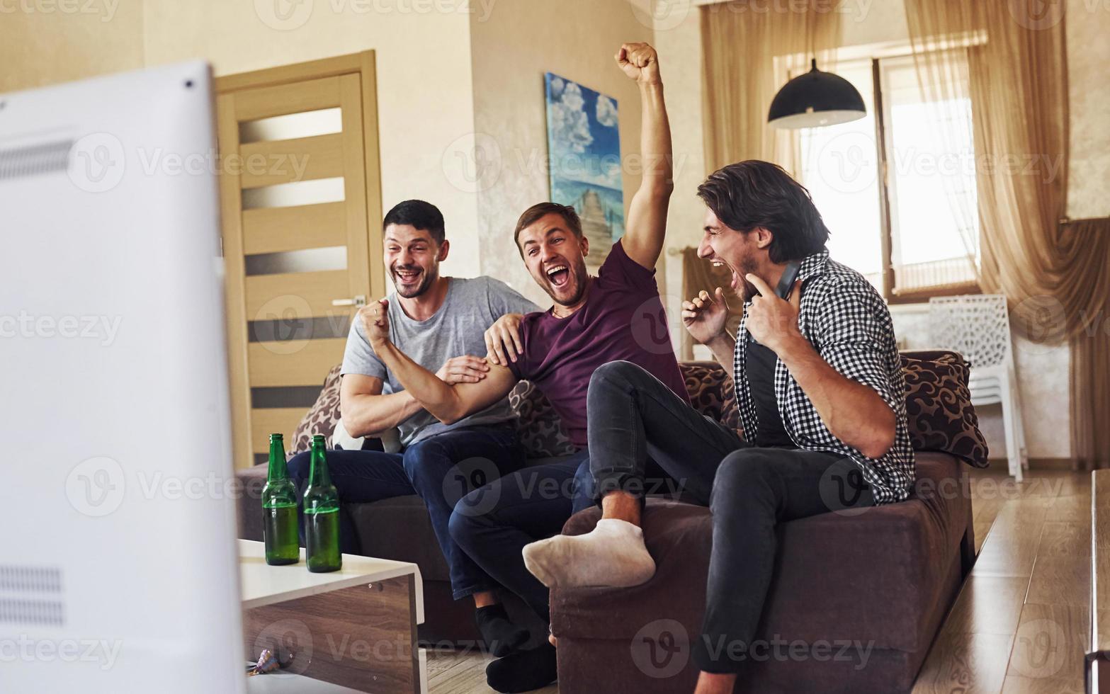 Celebrating victory. Excited three friends watching soccer on TV at home together photo
