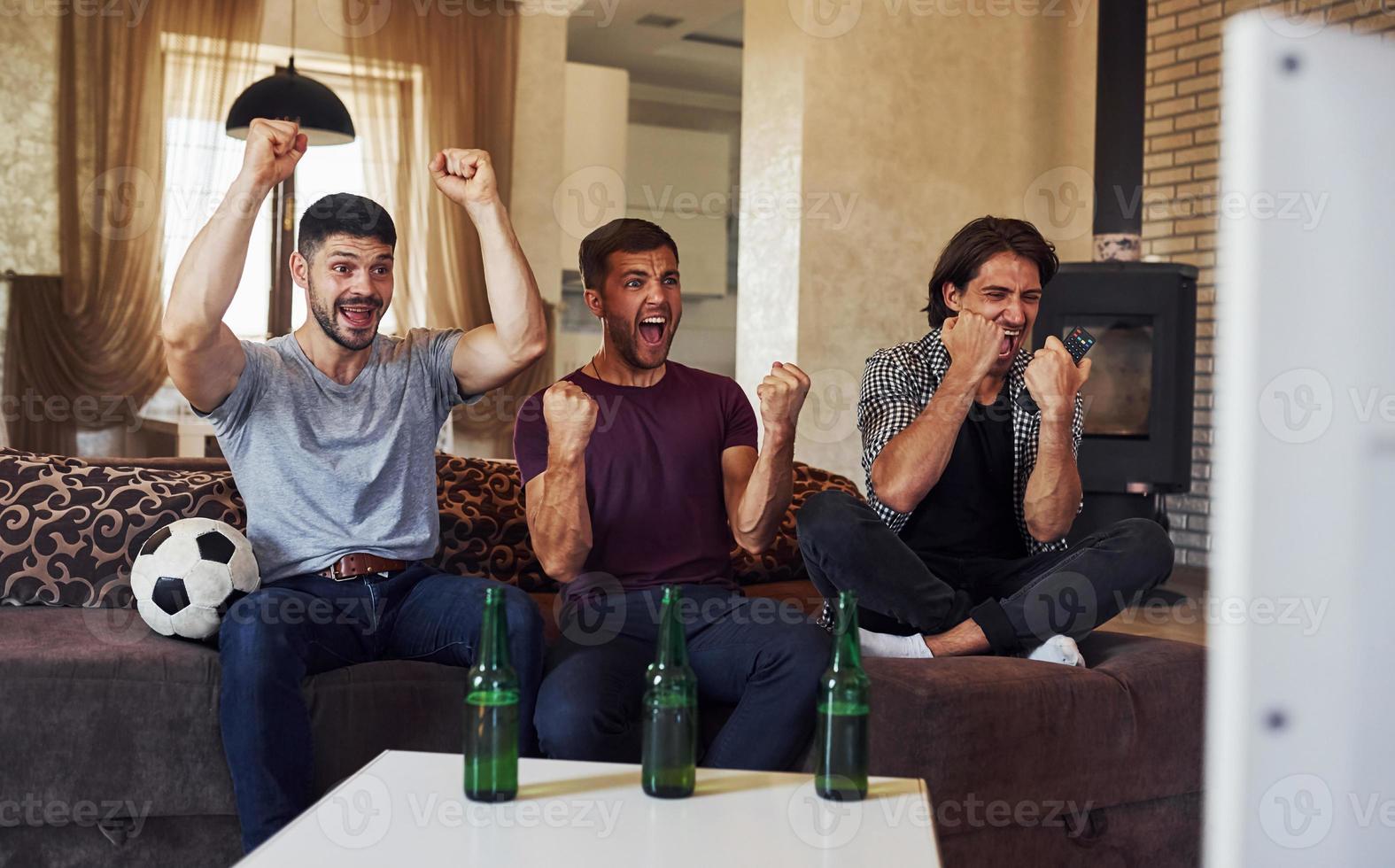 Celebrating victory. Excited three friends watching soccer on TV at home together photo