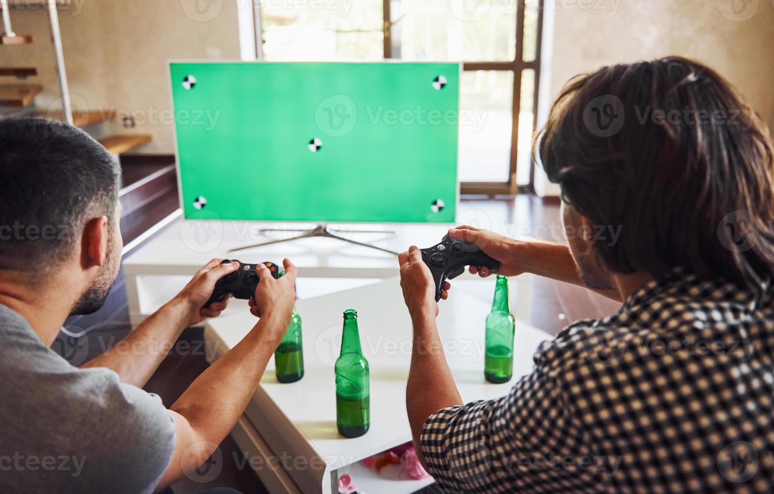 Beer on the table. Group of friends have fun playing console game indoors at living room photo