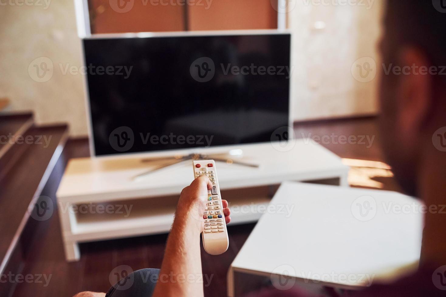 Backing view of man holds remote controller in hand and turning on TV photo