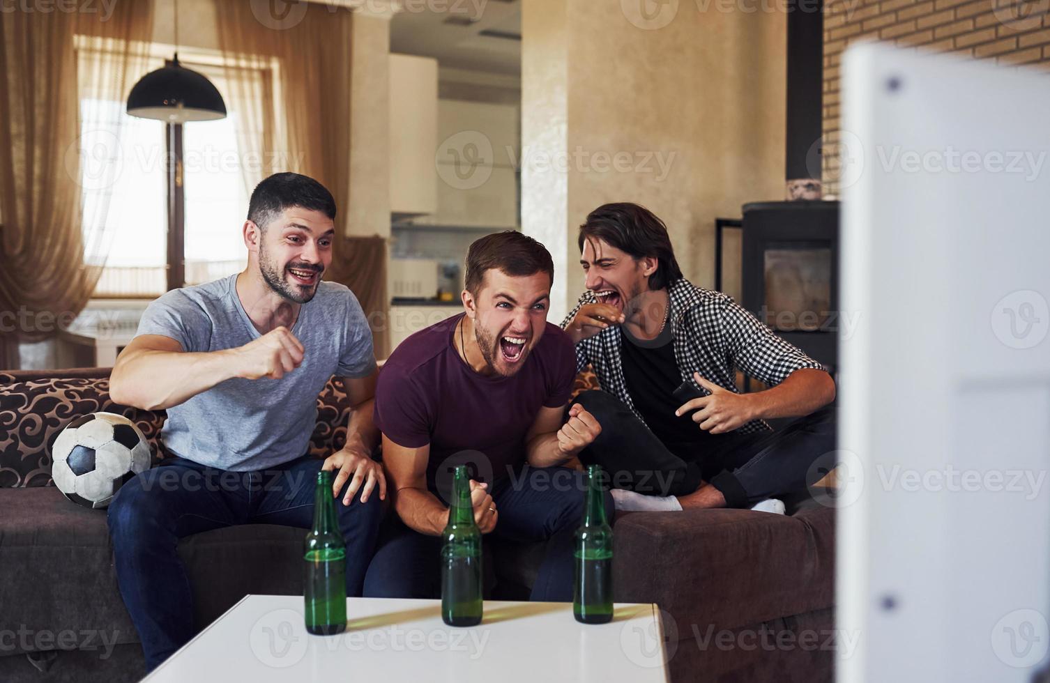 Celebrating victory. Excited three friends watching soccer on TV at home together photo