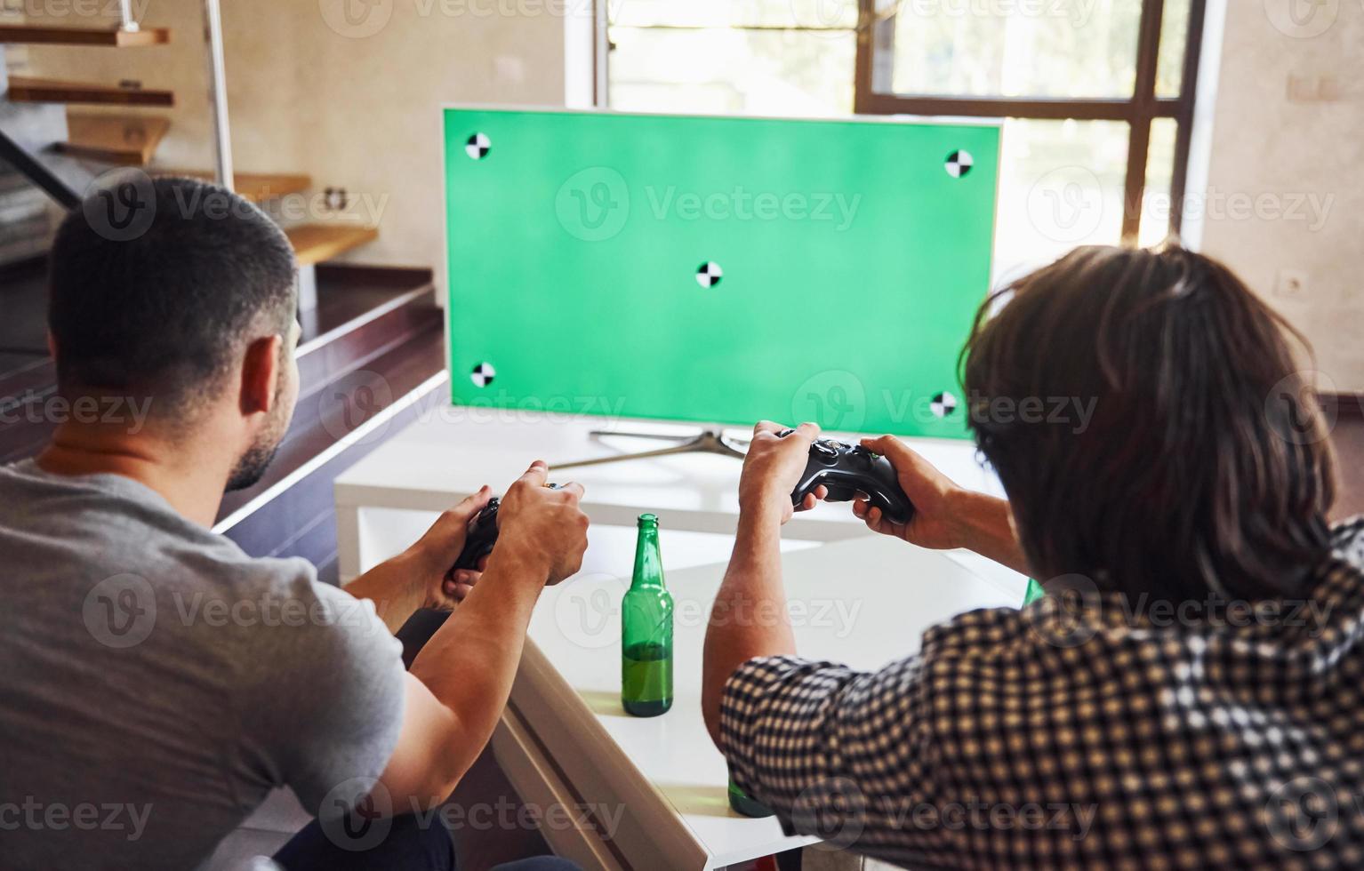 cerveza en la mesa. grupo de amigos se divierten jugando juegos de consola en el interior de la sala de estar foto