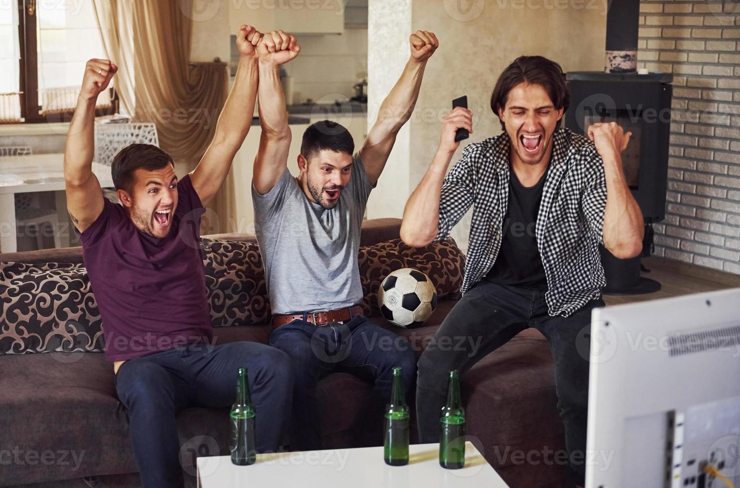 It's a goal. Excited three friends watching soccer on TV at home together photo