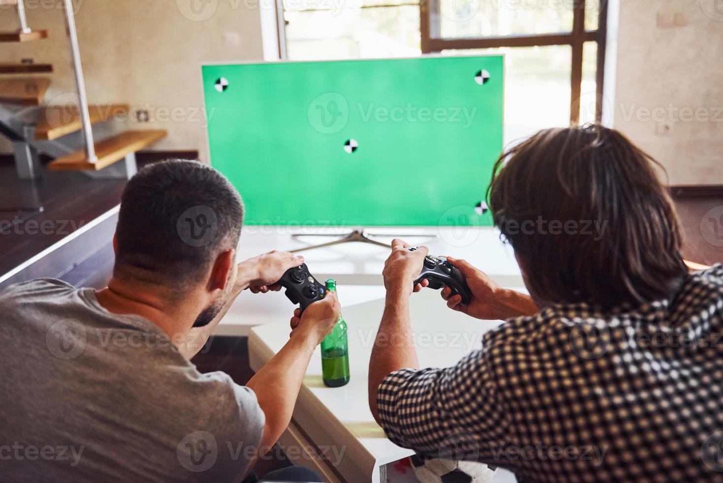 cerveza en la mesa. grupo de amigos se divierten jugando juegos de consola en el interior de la sala de estar foto