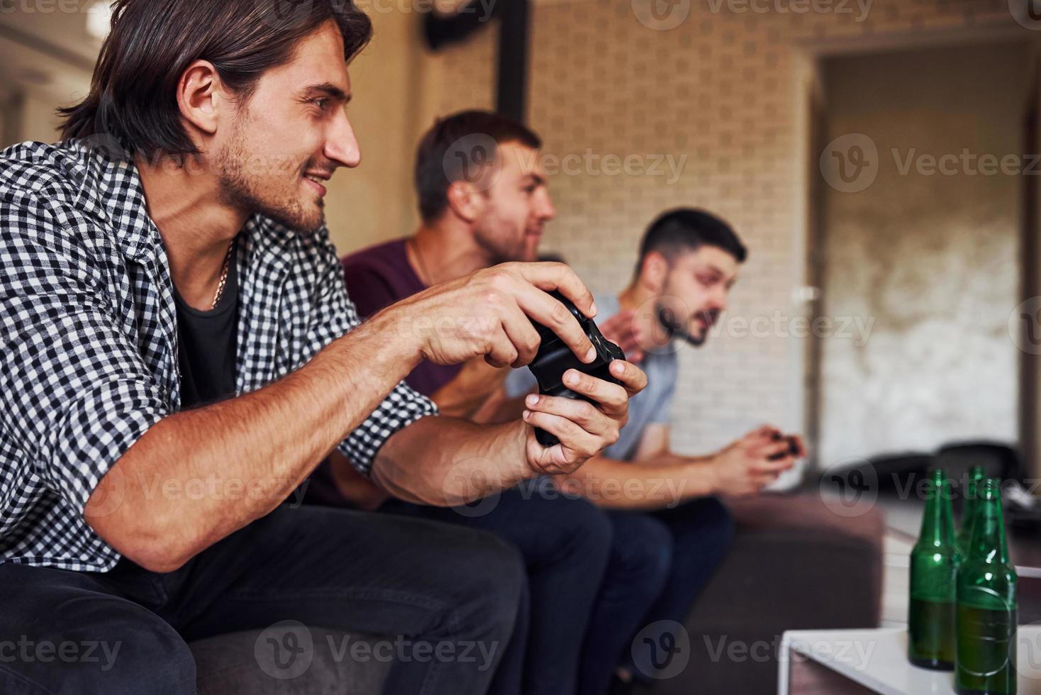 Side view. Group of friends have fun playing console game indoors at living room photo