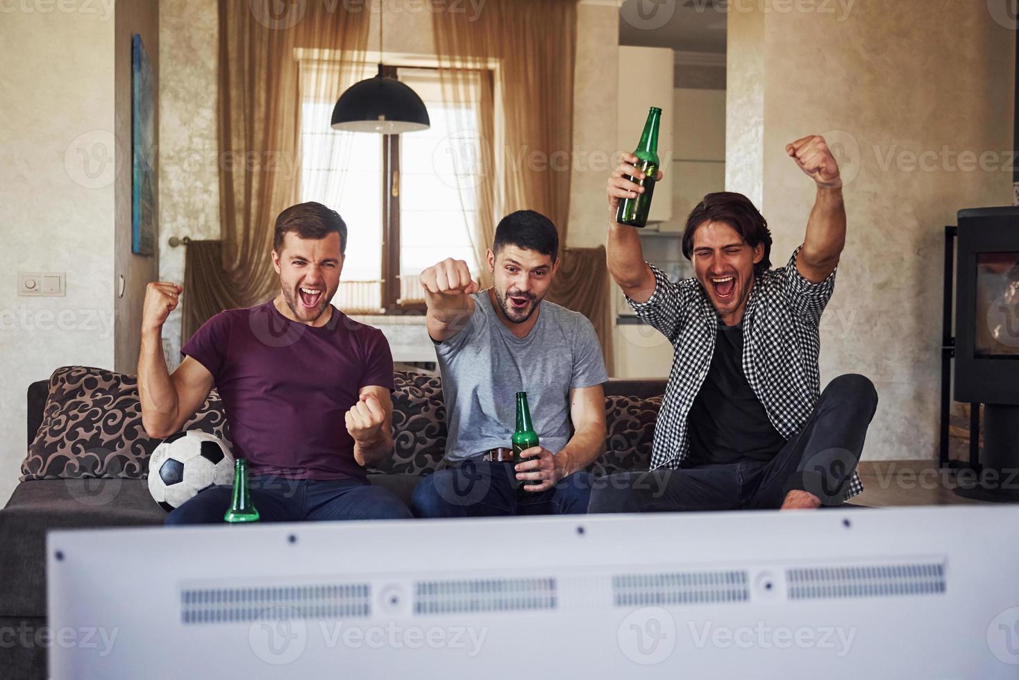 It's a goal. Excited three friends watching soccer on TV at home together photo