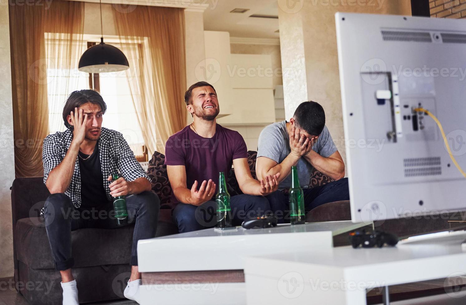 It's a defeat. Sad three friends watching soccer on TV at home together photo