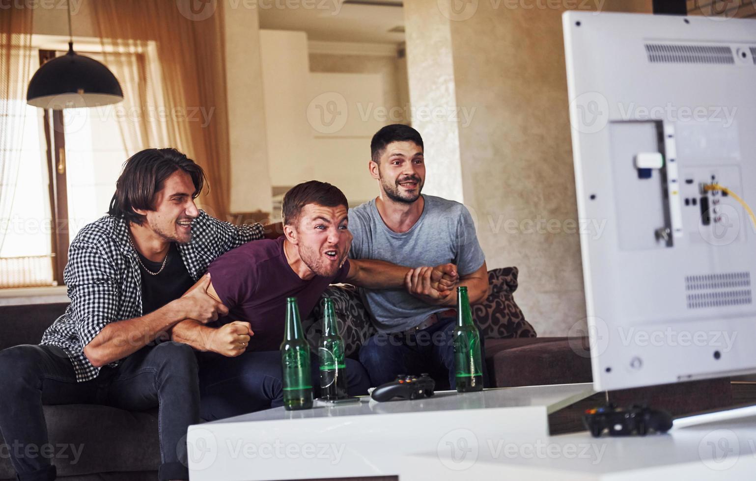 Excited three friends watching soccer on TV at home together photo