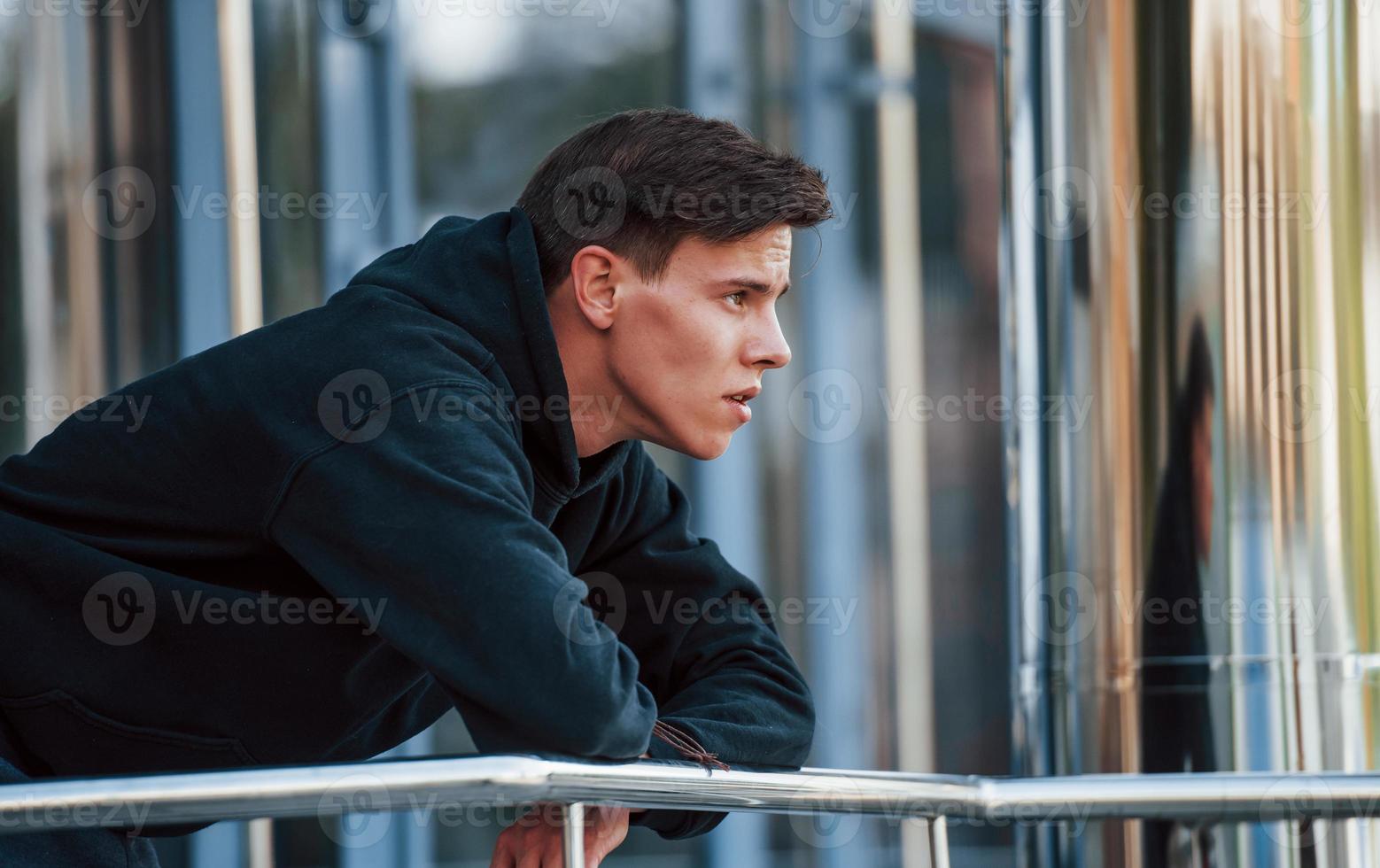 Portrait of young main in black clothes that leaning on the railings and taking a break photo