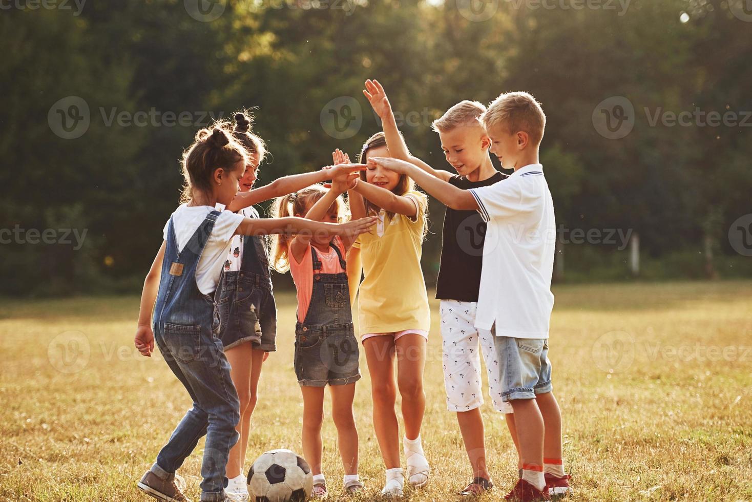 Ready for the game. Young sportive kids with soccer ball stands together in the field at sunny day photo